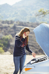 Woman talking on cell phone with automobile hood raised at roadside - CAIF16930