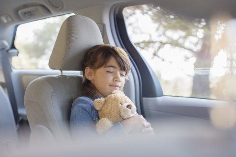 Girl with teddy bear sleeping in back seat of car stock photo