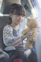 Girl with teddy bear in back seat of car - CAIF16950