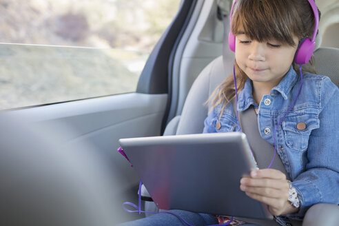 Mädchen mit Kopfhörern und digitalem Tablet auf dem Rücksitz eines Autos - CAIF16956