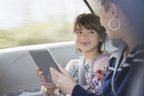 Glückliche Mutter und Tochter benutzen ein digitales Tablet auf dem Rücksitz eines Autos - CAIF16958