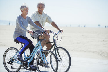 Senior couple riding bicycles on beach boardwalk - CAIF16984