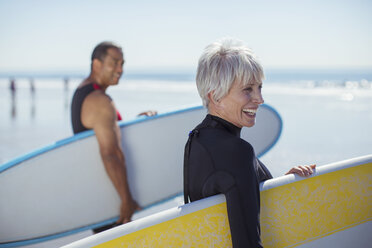 Älteres Paar trägt Surfbretter am Strand - CAIF16991