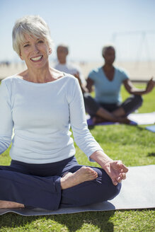 Porträt einer lächelnden älteren Frau, die im Park Yoga praktiziert - CAIF16992