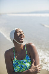 Woman in bathing suit and cap laughing on beach - CAIF17002