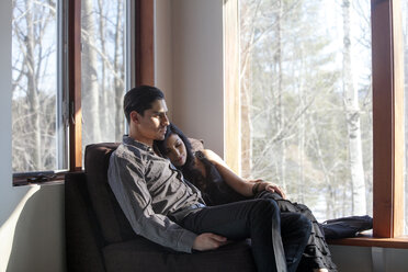 Paar entspannt sich auf einem Stuhl am Fenster zu Hause - CAVF08774