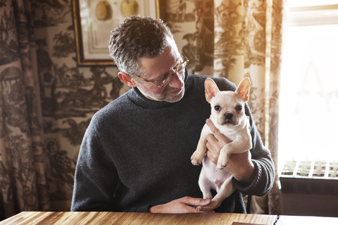 Mann sieht französische Bulldogge an, während er zu Hause am Tisch sitzt, lizenzfreies Stockfoto