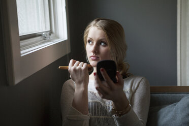 Girl looking away while holding make-up brush at home - CAVF08831