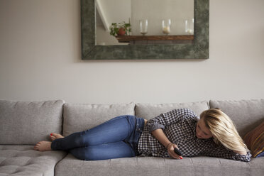 Mädchen in voller Länge bei der Benutzung eines Smartphones, während sie zu Hause auf dem Sofa liegt - CAVF08844