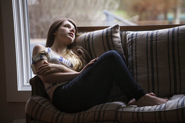 Girl looking away while relaxing on sofa at home - CAVF08846