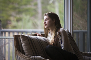 Teenager-Mädchen schaut weg, während sie zu Hause auf dem Sofa sitzt - CAVF08847