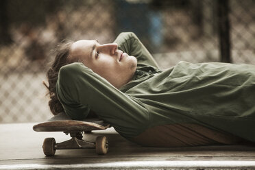 Seitenansicht eines Mannes, der sich mit dem Kopf auf ein Skateboard im Skateboardpark stützt - CAVF08859