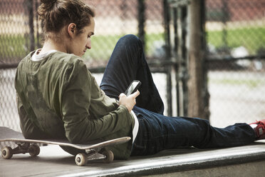 Mann benutzt sein Smartphone, während er sich auf einem Sitz im Skateboard-Park entspannt - CAVF08861