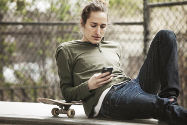 Mann benutzt Mobiltelefon, während er auf einem Sitz im Skateboard-Park sitzt - CAVF08862