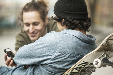 Freunde schauen auf ihr Handy, während sie sich im Skateboardpark entspannen - CAVF08867