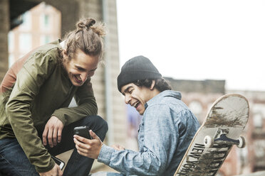 Glückliche Freunde schauen im Skateboard-Park auf ihr Smartphone - CAVF08868