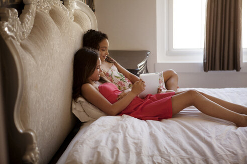 Geschwister benutzen ein Tablet, während sie zu Hause im Bett sitzen - CAVF08893
