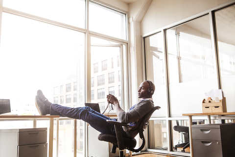 Seitenansicht eines Geschäftsmannes mit Kopfhörern, der auf einem Stuhl im Büro sitzt, lizenzfreies Stockfoto