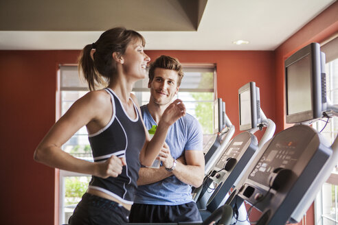 Mann betrachtet Frau, die auf dem Laufband im Fitnessstudio läuft - CAVF08977