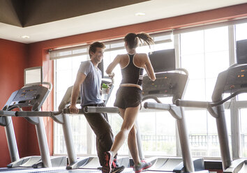 Happy man looking at woman running on treadmill at gym - CAVF08978