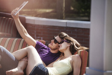 Happy couple taking selfie while sitting on sofa at backyard - CAVF08991