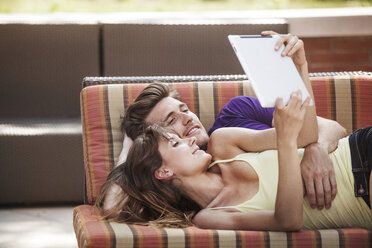 Happy couple using tablet while lying on sofa at backyard - CAVF08993