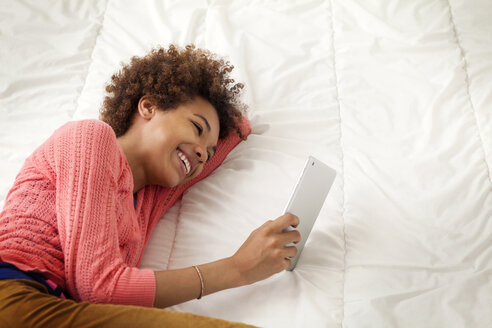 Glückliches Mädchen hält Tablet-Computer, während sie auf dem Bett zu Hause liegt - CAVF09005