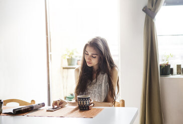 Woman using mobile phone while sitting at table in home - CAVF09026