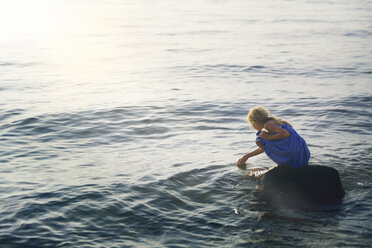 Girl crouching on rock in sea - CAVF09034