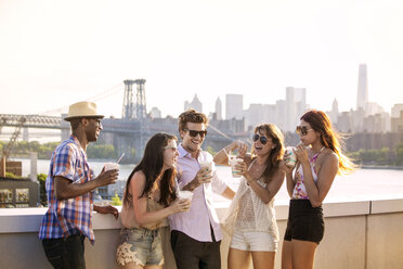 Happy friends drinking iced coffee while standing on building terrace against Williamsburg Bridge - CAVF09044