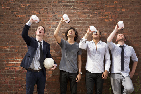 Freunde trinken Wasser, während sie an einer Mauer stehen - CAVF09054