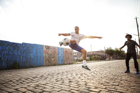 Mann kickt Fußball, während sein Freund auf die Straße schaut - CAVF09069