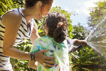 Low angle view of mother with daughter splashing water from garden hose - CAVF09077