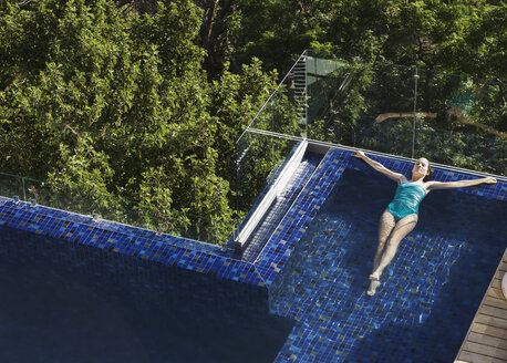 Woman floating in luxury swimming pool - CAIF17086