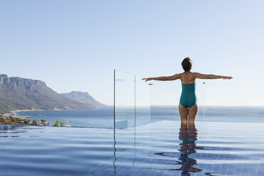 Woman basking in infinity pool overlooking ocean - CAIF17089