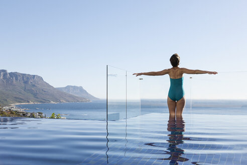 Woman basking in infinity pool overlooking ocean - CAIF17089