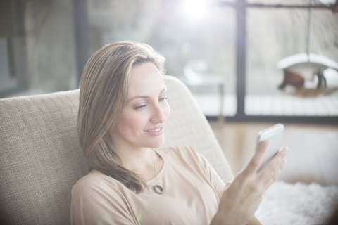 Frau benutzt Mobiltelefon auf Sofa, lizenzfreies Stockfoto