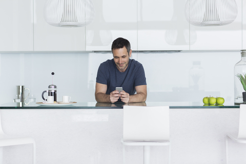 Mann benutzt Mobiltelefon in moderner Küche, lizenzfreies Stockfoto