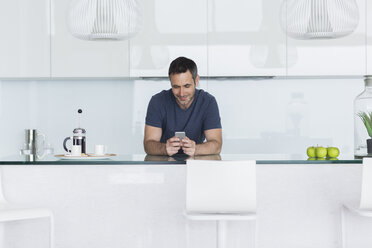 Man using cell phone in modern kitchen - CAIF17149