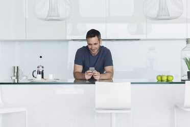 Mann benutzt Mobiltelefon in moderner Küche - CAIF17149