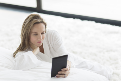 Woman in bathrobe using digital tablet in bedroom stock photo