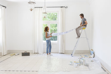 Couple laying out wallpaper together - CAIF17240