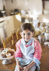 Young girl sitting on kitchen table near cupcakes - CAIF17253