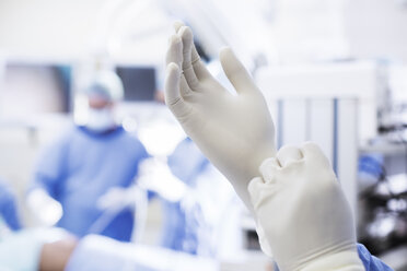 Nahaufnahme eines Chirurgen, der im Operationssaal chirurgische Handschuhe anzieht - CAIF17401