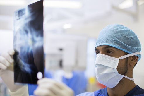 Nahaufnahme eines Chirurgen mit chirurgischer Kappe und Maske, der eine Röntgenaufnahme im Operationssaal betrachtet - CAIF17412