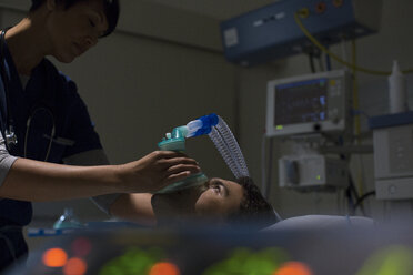 Arzt hält Sauerstoffmaske über das Gesicht eines Patienten auf der Intensivstation - CAIF17413