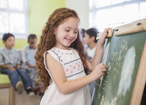 Schülerin zeichnet auf Kreidetafel im Klassenzimmer, lizenzfreies Stockfoto