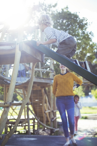 Lehrer beobachtet Schüler beim Spielen auf dem Spielgerät, lizenzfreies Stockfoto