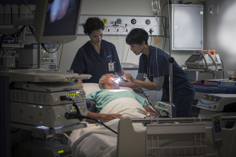 Reife Ärztin und Krankenschwester untersuchen den Rachen eines Patienten, lizenzfreies Stockfoto