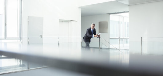 Businessman standing at railing in office - CAIF17607